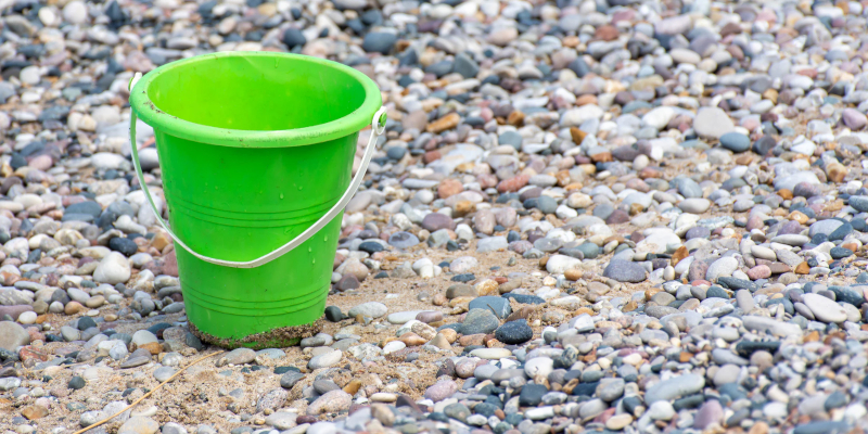 A bucket on top of a beach with lots of different pebbles