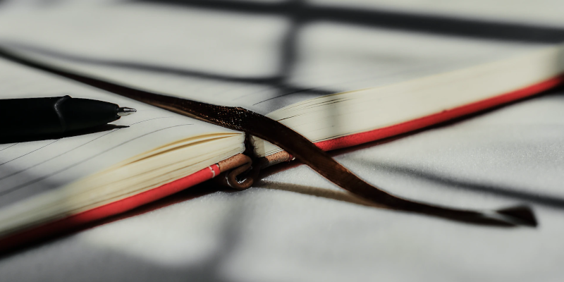 A notebook open on an empty page, with a pen and bookmark on top